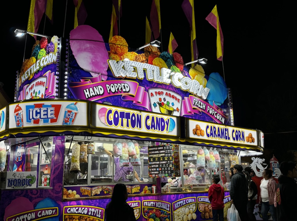A Pop Above’s brightly illuminated flagship stand with colorful popcorn signage and guests at the counter